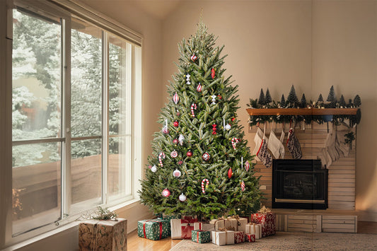 A decorated Fraser fir tree stands in the corner of a neutrally-decorated room, next to a large window and a fireplace. There are presents scattered underneath the tree.